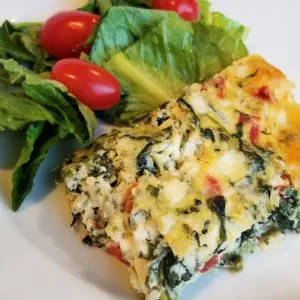 Piece of Italian spinach pie on white plate with green salad and tomatoes