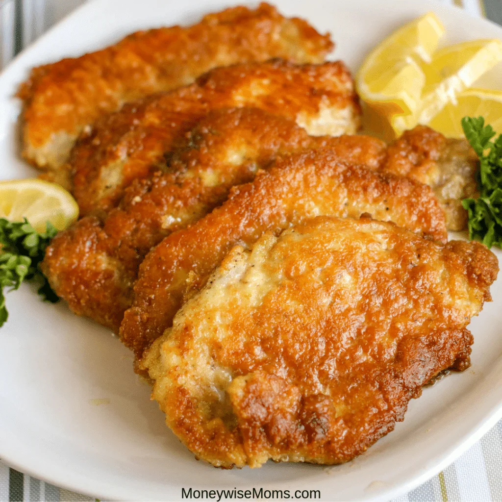 finished pork milanese on a plate with lemon wedges.