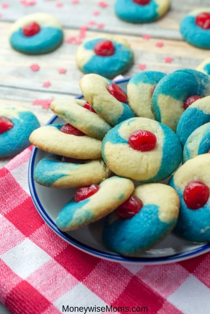 tall image of finished patriotic thumbprint cookies in a bowl with a red plaid tablecloth underneath. 