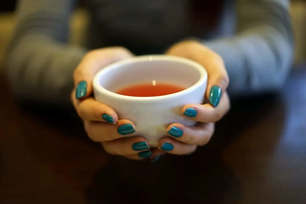 womans hands holding white cup of tea