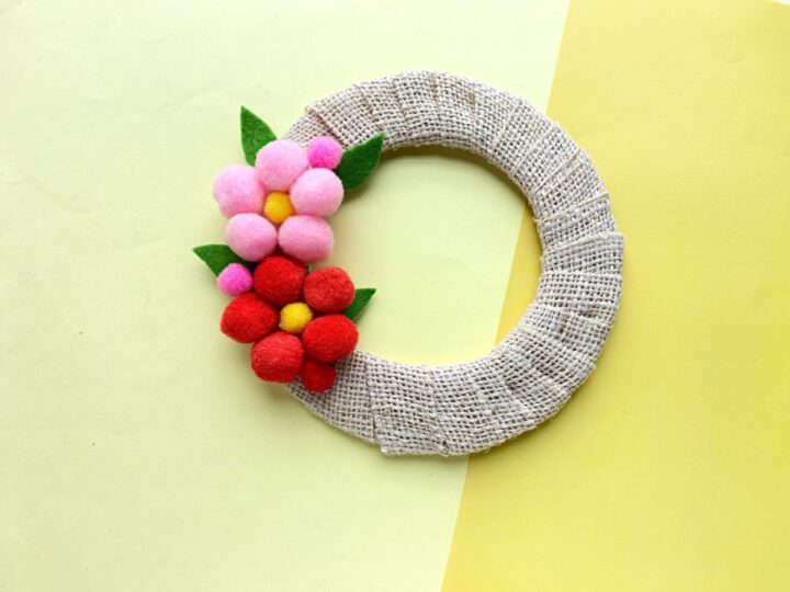 This beautiful pom pom wreath makes a great Mother's Day gift. It's a cute, DIY project you can make at home with very little in materials or cost. This is a simple Mother's Day wreath that you can customize!