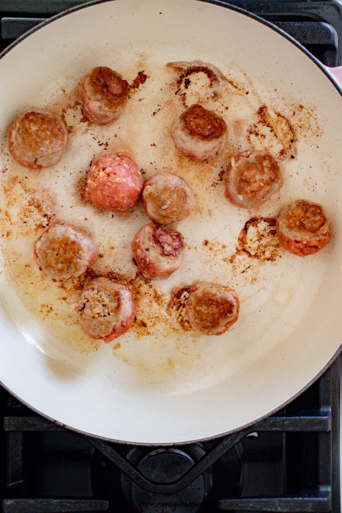 Image shows the meatballs being cooked in a frying pan. 