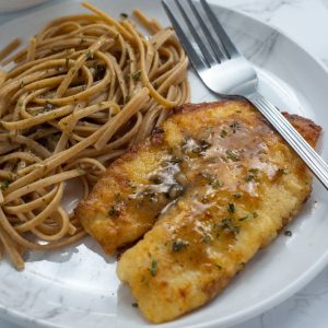 Lemon butter tilapia filet and noodles on white plate