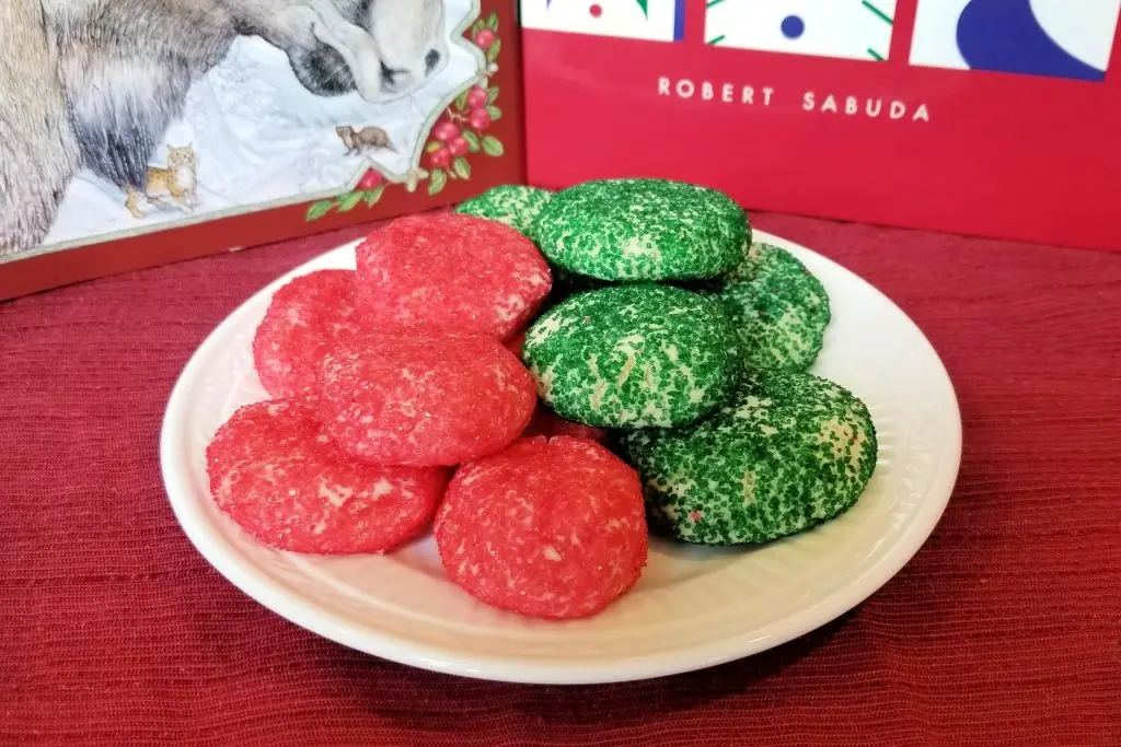White plate with green and red sugar sprinkle cookies in front of Christmas books