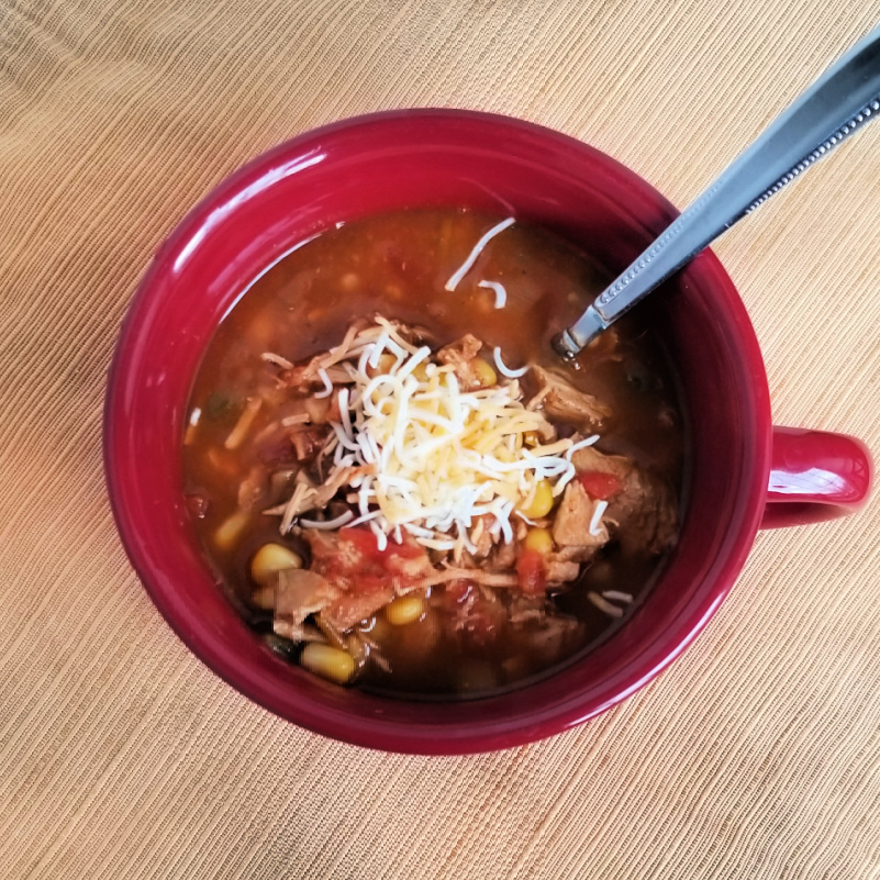 Slow cooker chicken tortilla soup in a red mug bowl on yellow placemat