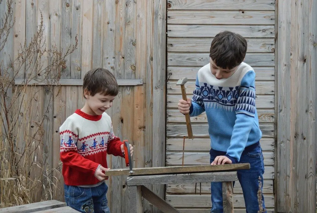 Two boys with clamp hammer and wood doing open buildilng