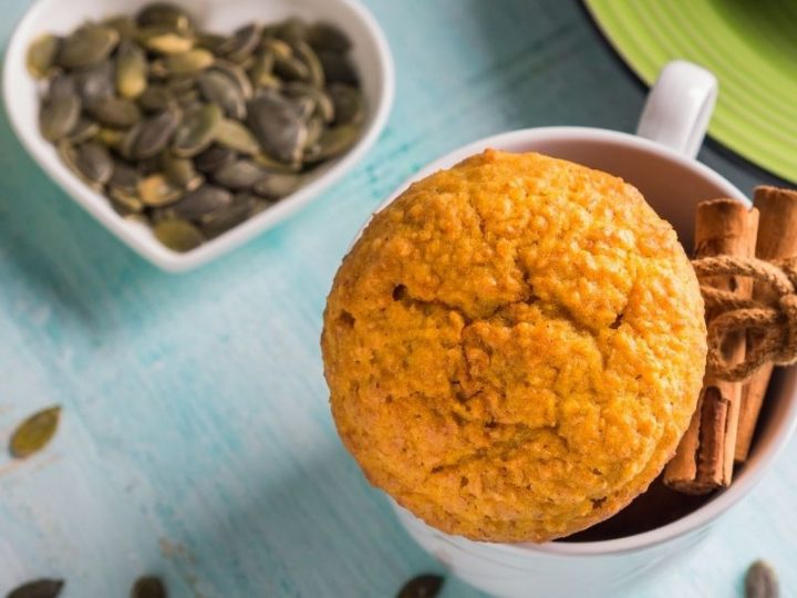 pumpkin wheat muffin in white mug next to bowl of pumpkin seeds
