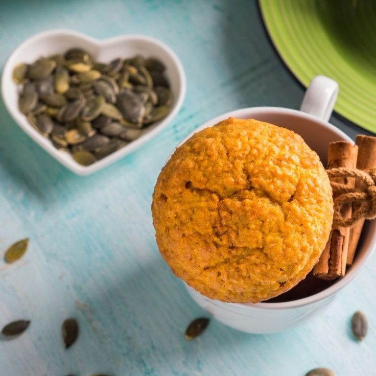 pumpkin wheat muffin in white mug next to bowl of pumpkin seeds