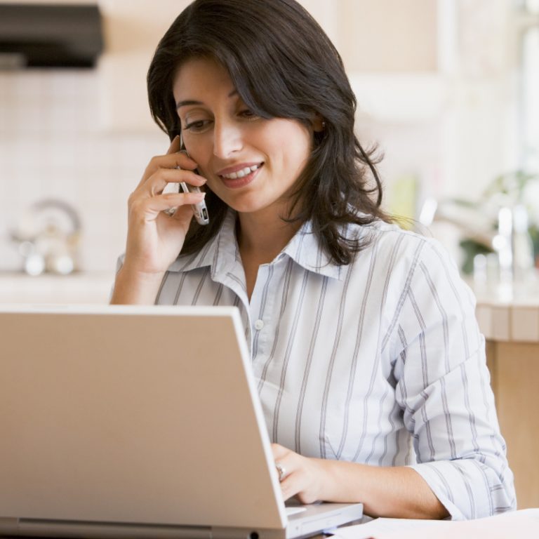 woman in kitchen with laptop using phone