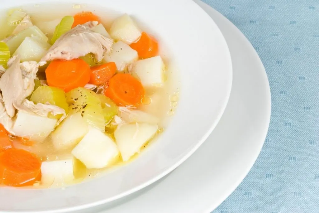 chicken potato soup recipe in white bowl on white plate on blue tablecloth