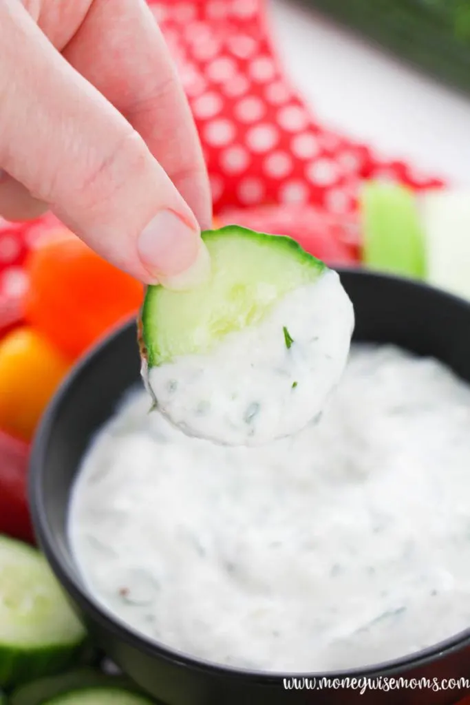 a cucumber being used to dip the tzatziki sauce for a snack. 