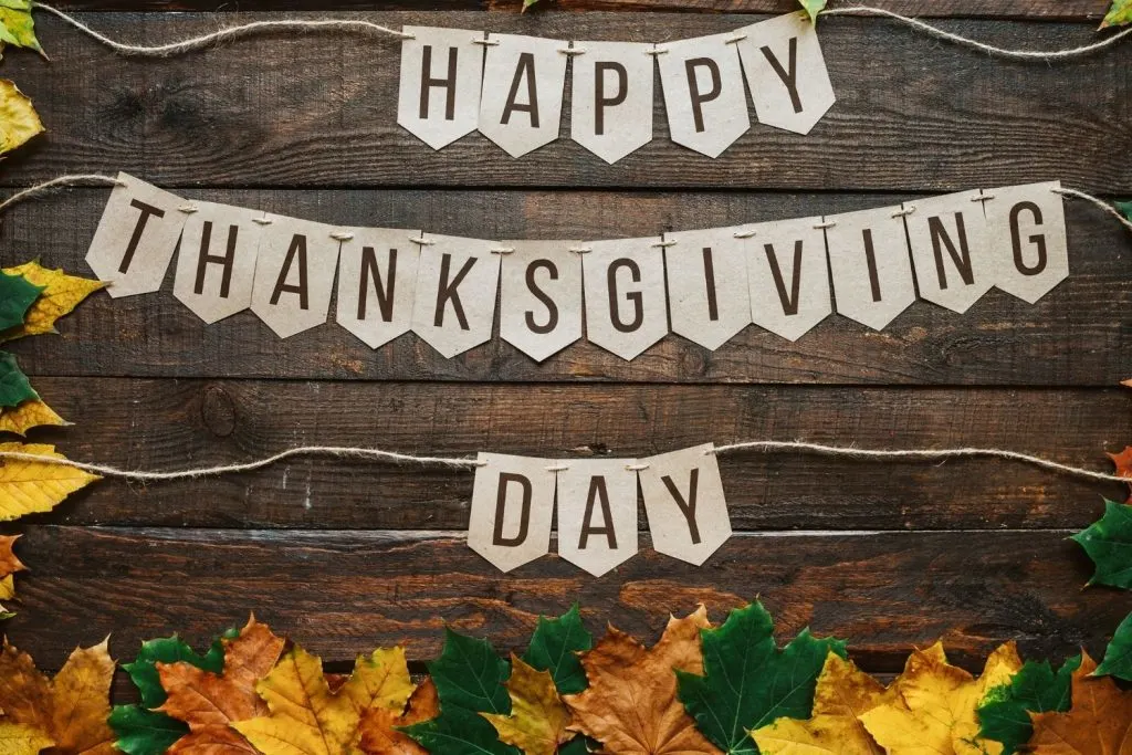 paper bunting flags that say Happy Thanksgiving Day on wooden background with leaves - Thanksgiving wall decoration ideas