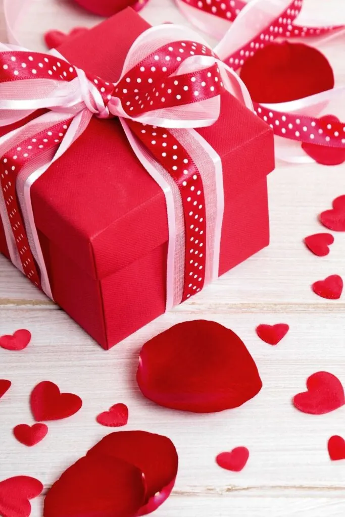red box wrapped with polka dot ribbon on white table with red rose petals - Valentine Gifts under $10