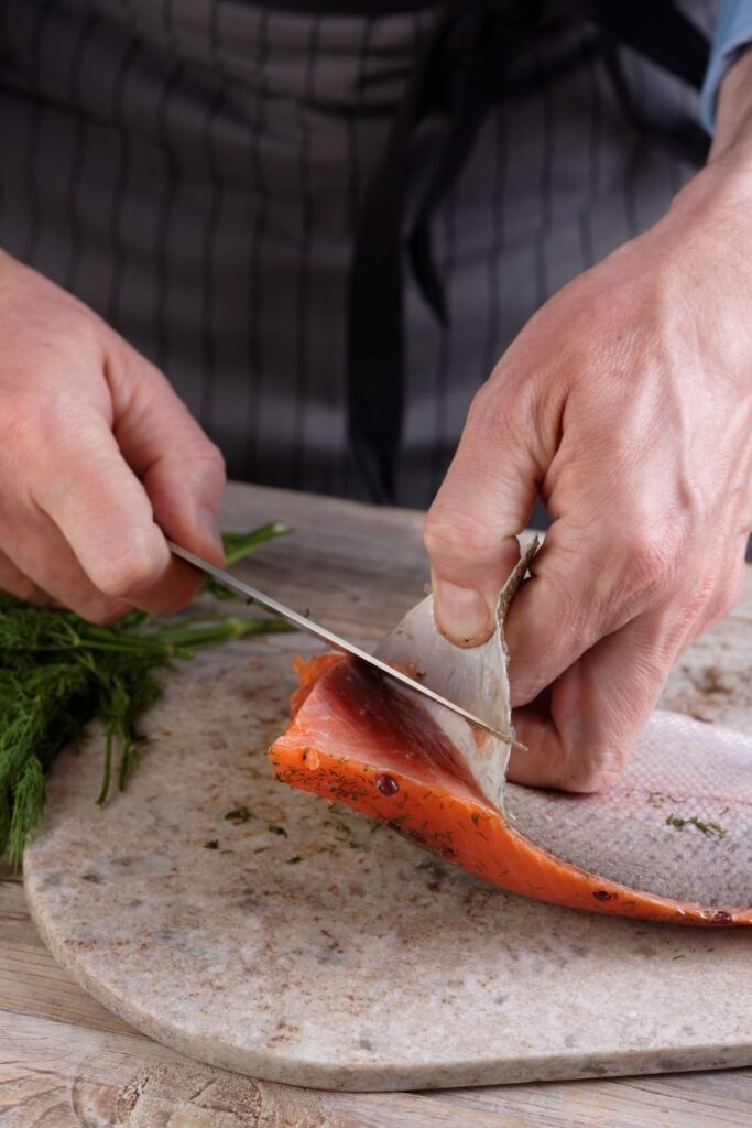 hands using knife to remove skin from salmon fillet before baking
