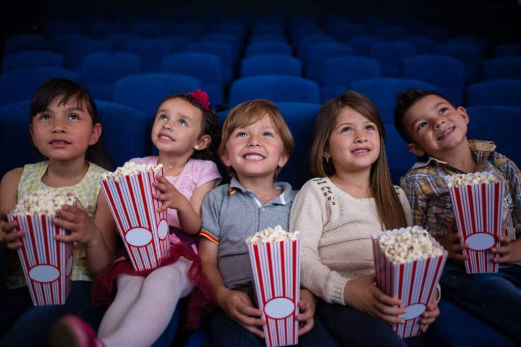 Five kids looking up at movie screen and holding popcorn