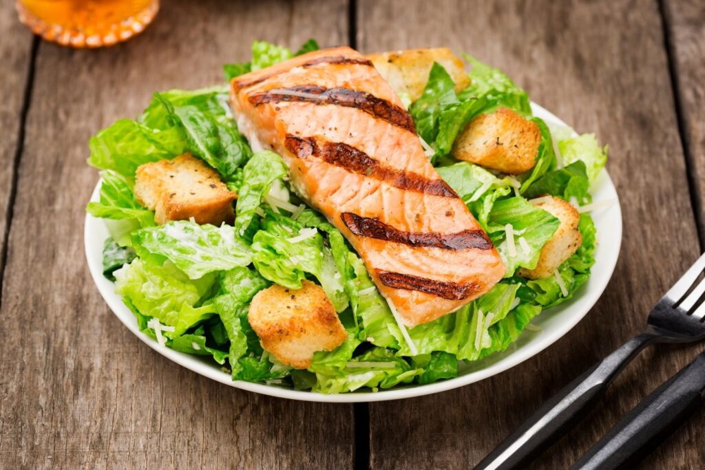 Grilled salmon fillet on bed or lettuce with croutons - white plate on wooden table