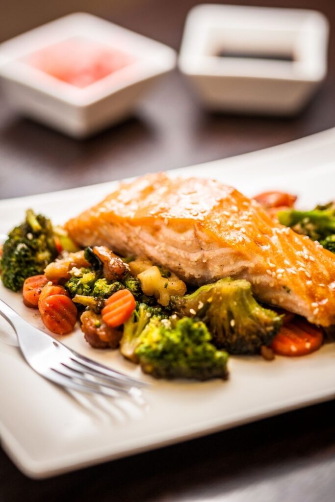 salmon fillet on top of mixed vegetables on white square plate