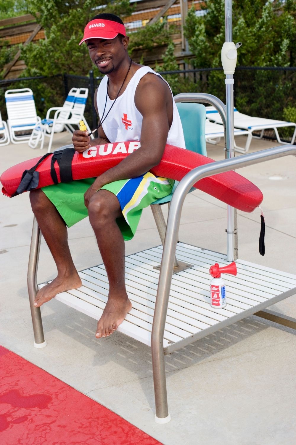Black male teen lifeguard in chair on pool deck