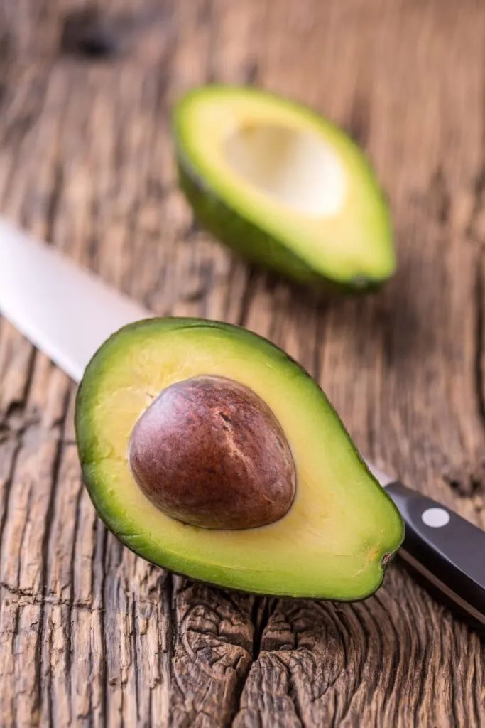 halved avocado on cutting board with knife