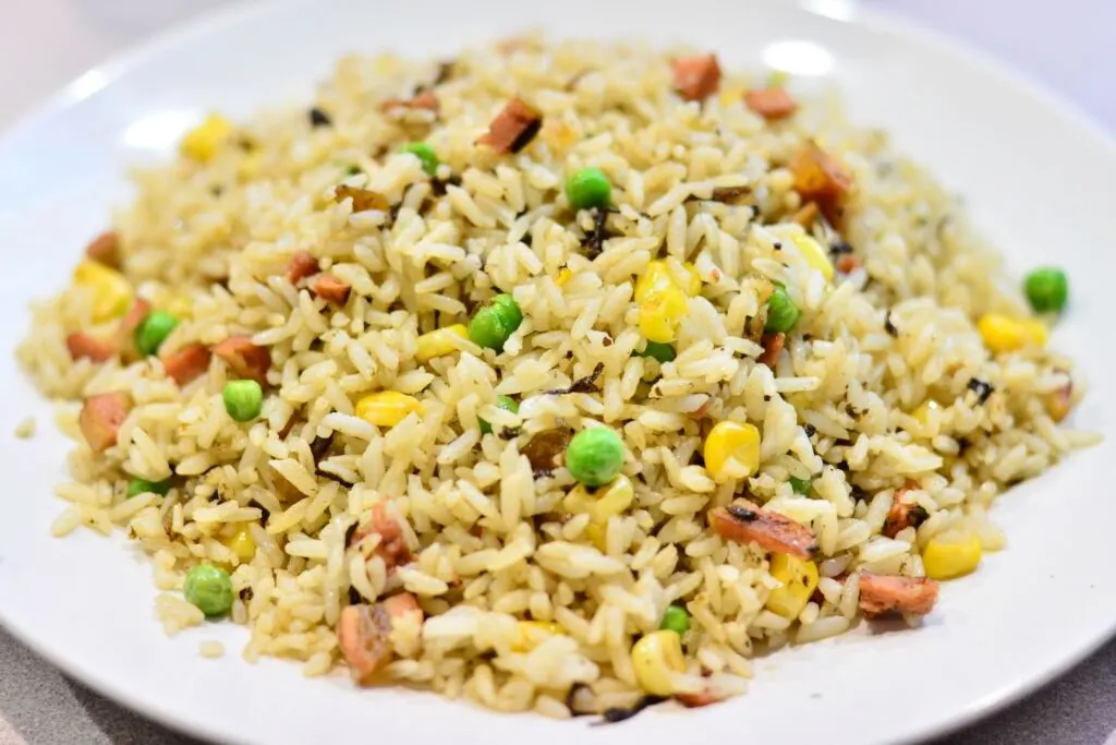 White plate of fried rice with peas and corn