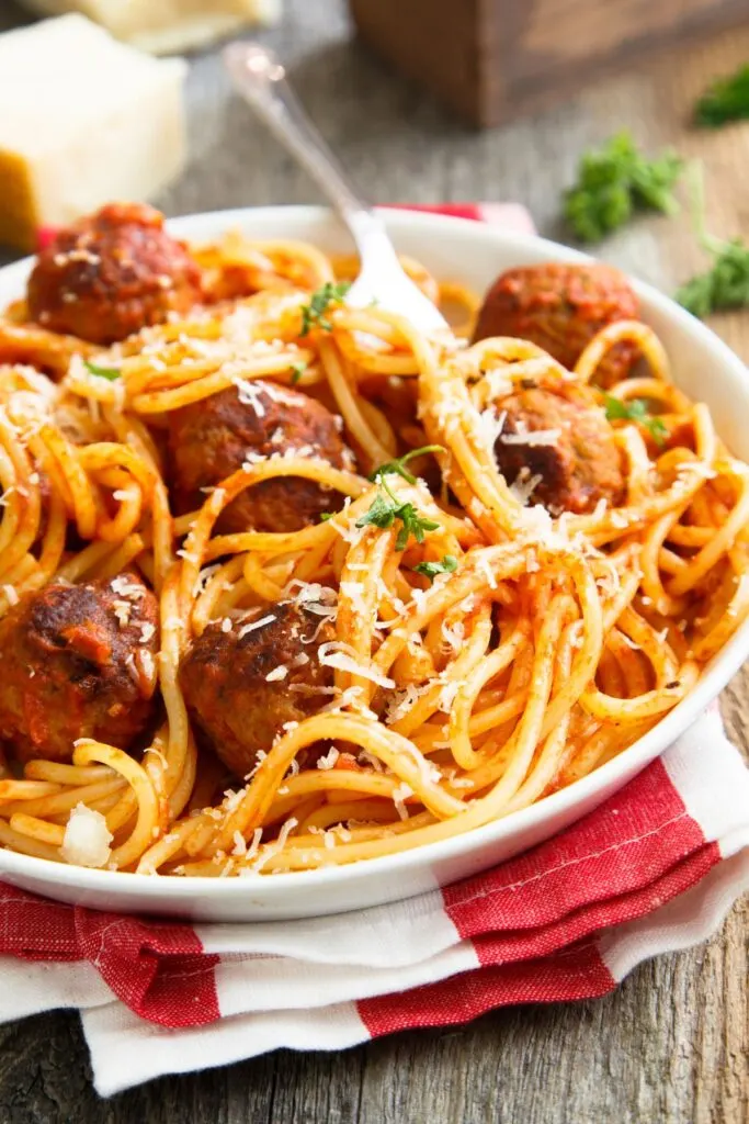 spaghetti and meatballs on white plate with red and white napkin