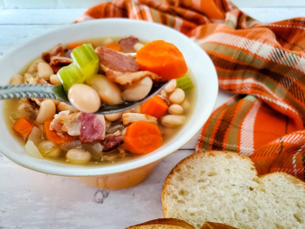 bean and bacon soup in white bowl with plaid napkin and bread