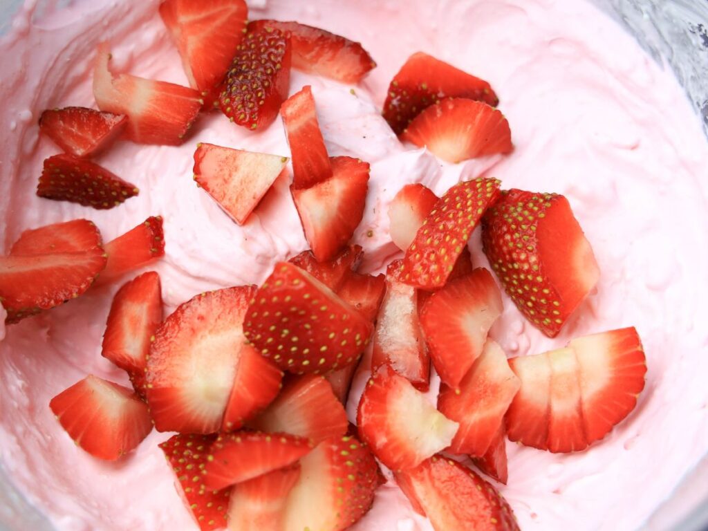 mixing cut strawberries into pink cream cheese mixture