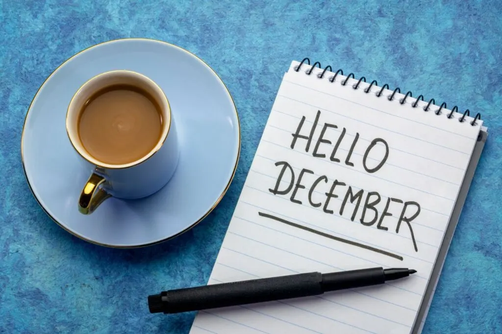 Hello December on notepad with black pen and blue cup of coffee on blue background