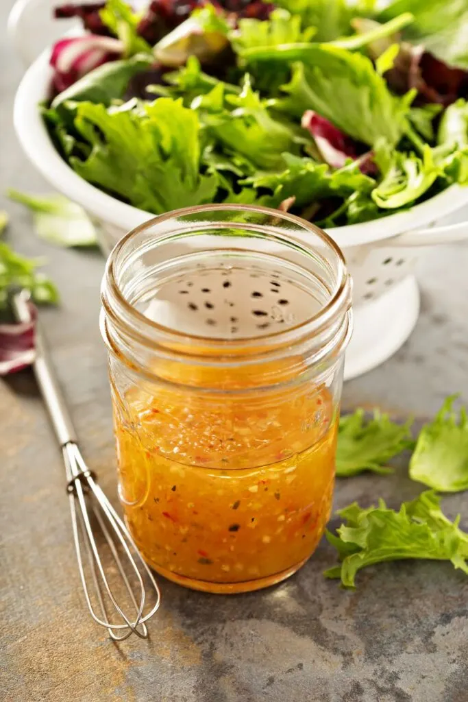 homemade Italian dressing in glass jar in front of lettuce in colander