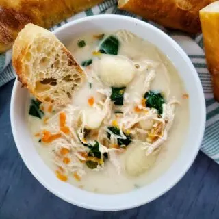 creamy gnocchi chicken soup in white bowl with piece of baguette