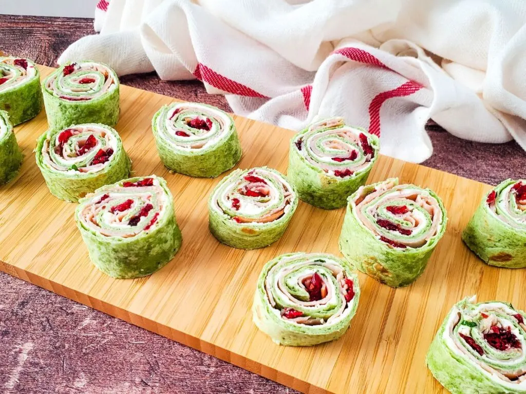 turkey rollups with cranberries on wooden board with white kitchen towel - turkey cranberry pinwheels