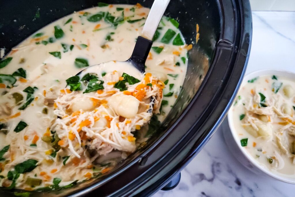 ladle full of chicken soup with gnocchi in black crock pot
