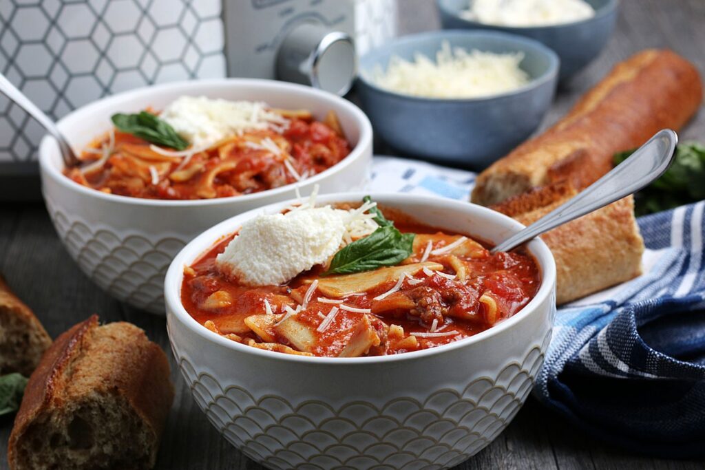 Two bowls lasagna soup with bread and toppings