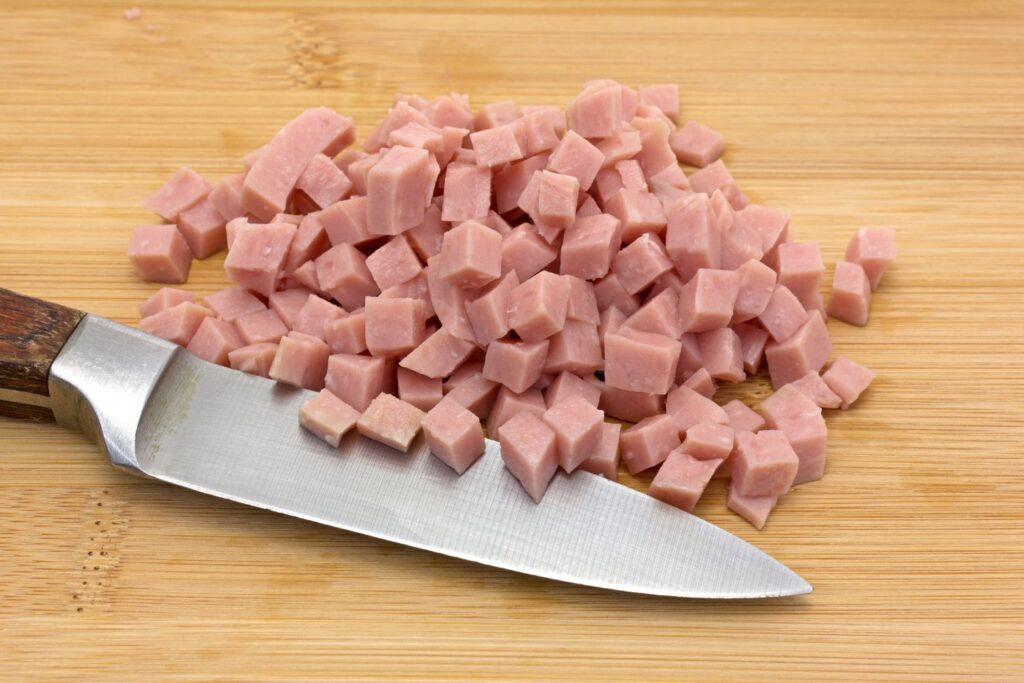 diced ham with knife on wooden cutting board